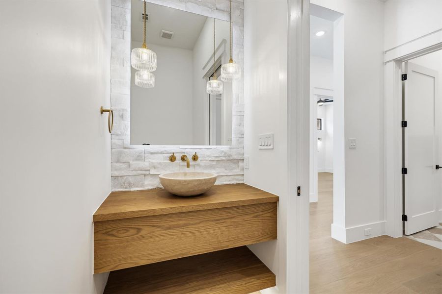 The powder room features a beautiful freestanding sink, a shimmer stone wall, and a backlit mirror for perfect pictures!