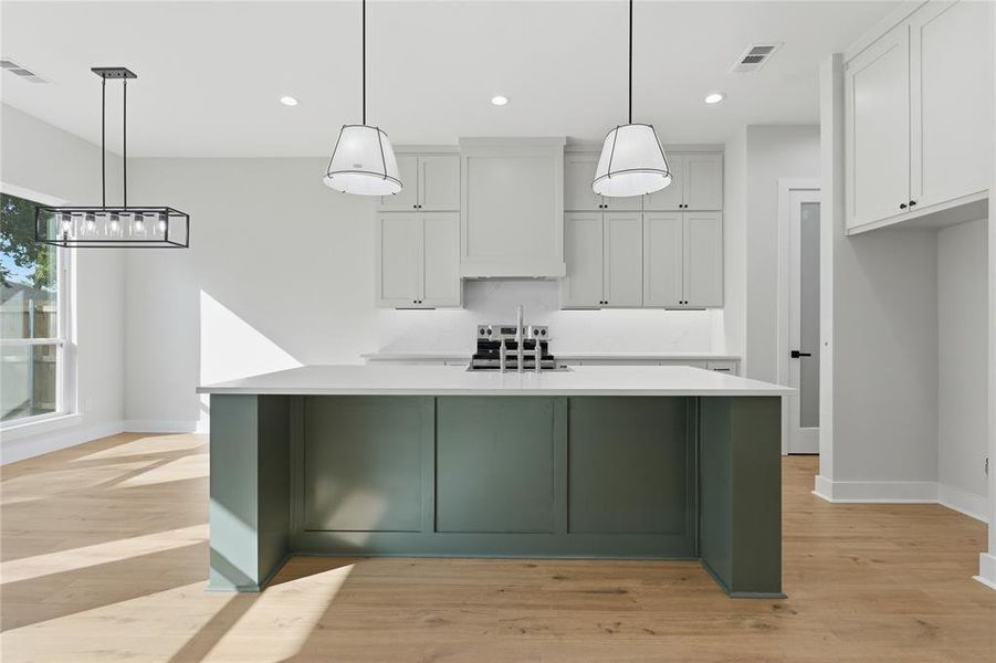 Modern kitchen featuring a spacious island with a light countertop, light-toned cabinetry, and wood-finish flooring Modern kitchen featuring a spacious island with a light countertop, light-toned cabinetry, and wood-finish flooring