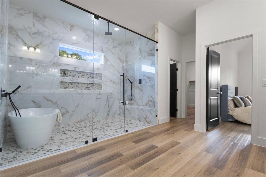 Bathroom with a spacious closet, a marble finish shower, a freestanding tub, and wood finished floors