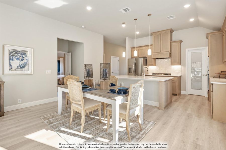 Open dining area with white table and light wood chairs next to kitchen island with pendant lights and light wood cabinets Open dining area with white table and light wood chairs next to kitchen island with pendant lights and light wood cabinets