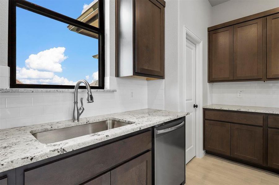 Kitchen featuring backsplash, dark brown cabinetry, sink, and stainless steel dishwasher