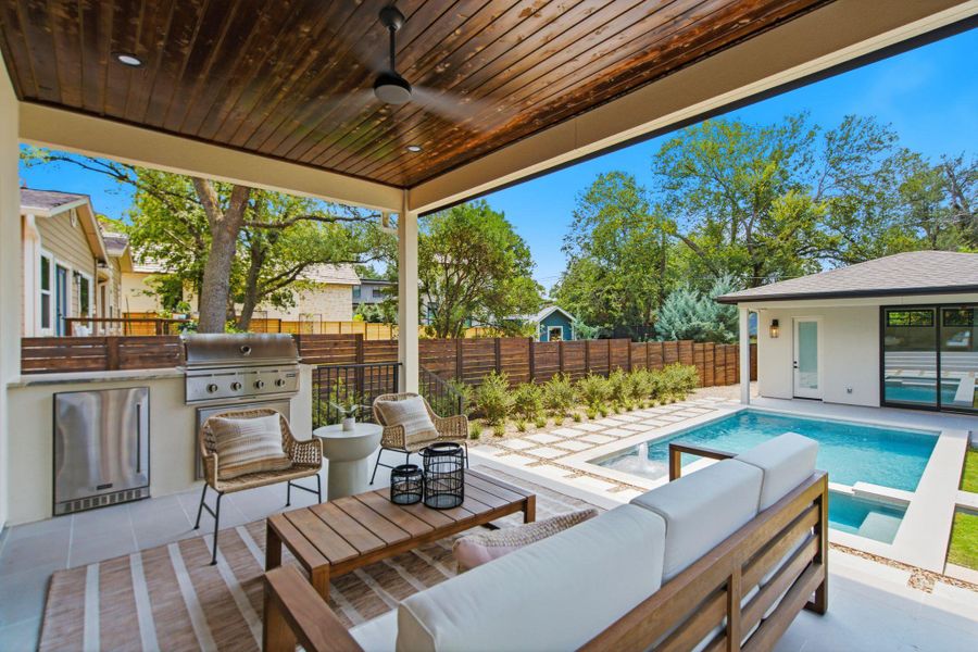 Rich wood ceilings shelter an outdoor kitchen overlooking a pristine pool and custom paver patio.