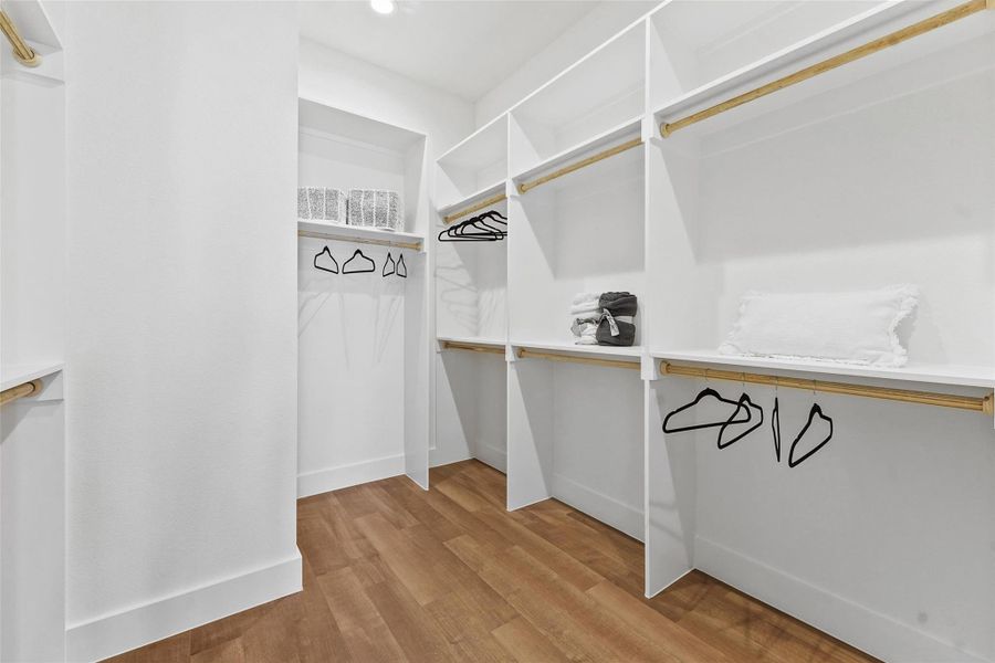 Spacious walk-in closet with built-in shelving, multiple hanging areas, and wood flooring for a clean, organized look. Spacious walk-in closet with built-in shelving, multiple hanging areas, and wood flooring for a clean, organized look.