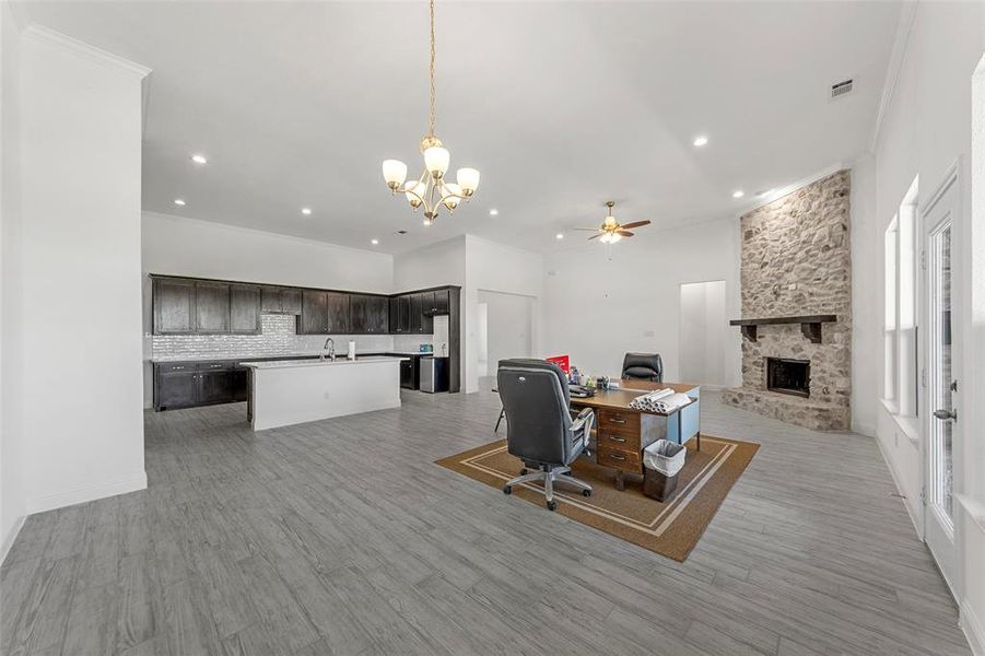 Home office featuring a chandelier, a stone fireplace, ornamental molding, a sink, and a ceiling fan