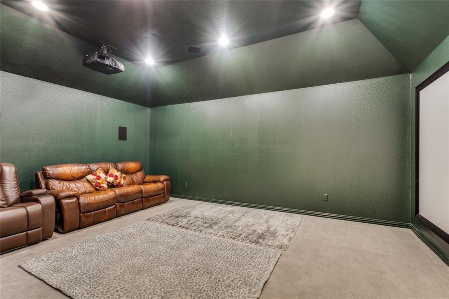 Cinema room with vaulted ceiling, carpet flooring, and a textured wall