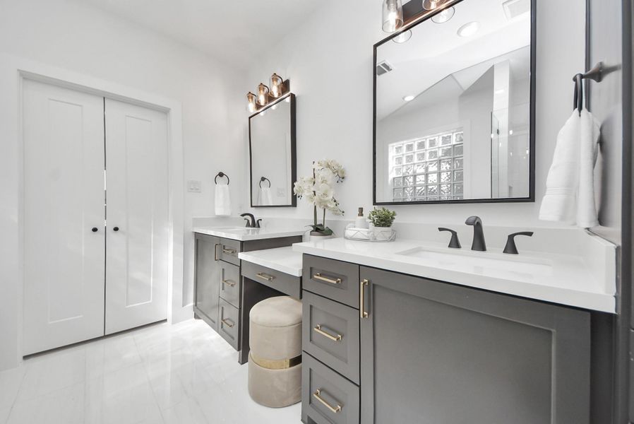 This bathroom features a sleek double vanity with black fixtures and ample storage. Neutral tones, large mirrors, and contemporary lighting contribute to a bright, elegant environment.
