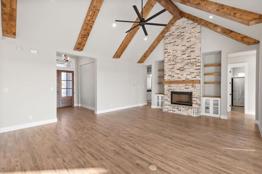 Unfurnished living room featuring high vaulted ceiling, wood-type flooring, beamed ceiling, and a brick fireplace