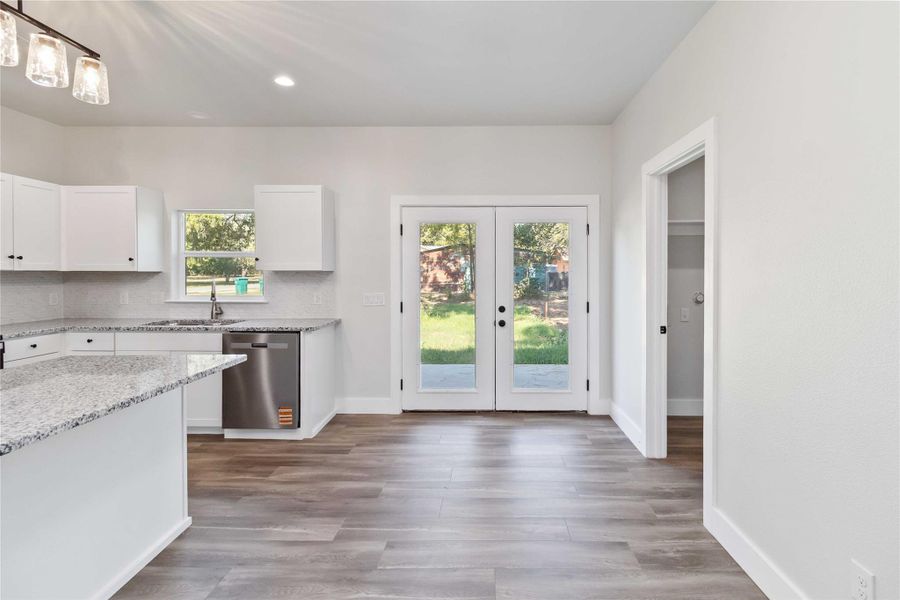 Kitchen featuring white cabinetry, french doors, light stone counters, stainless steel dishwasher, and recessed lighting