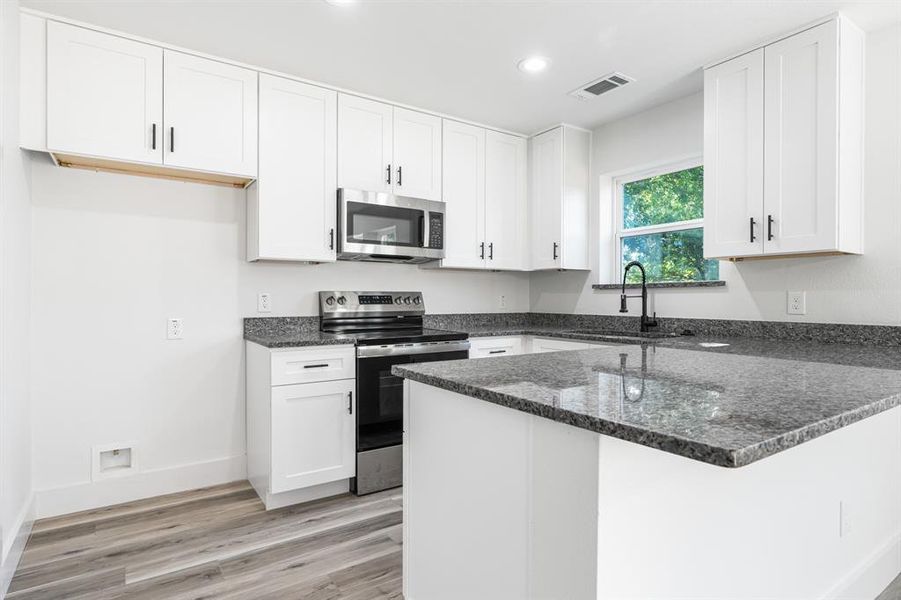 Kitchen with a peninsula, stainless steel appliances, dark stone counters, white cabinets, and recessed lighting