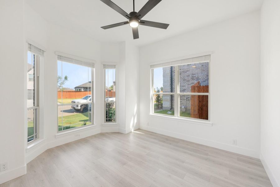 Empty room with light wood floors, ceiling fan, and multiple large windows with natural light Empty room with light wood floors, ceiling fan, and multiple large windows with natural light