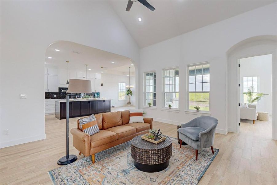 Living room with high vaulted ceiling, ceiling fan, and light hardwood / wood-style floors