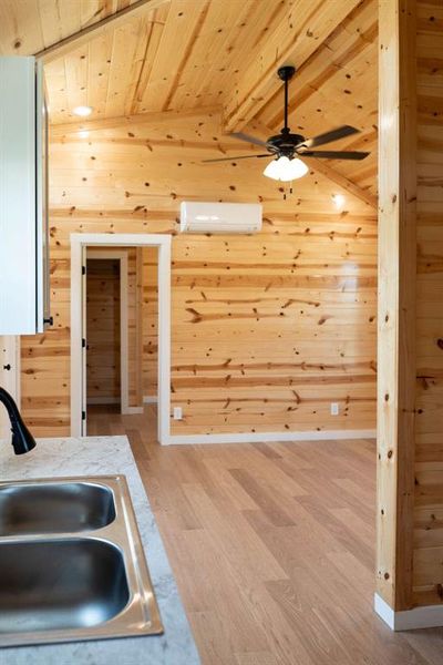 Kitchen with a wood ceiling with exposed beams, light wood-style floors, wooden walls, ceiling fan, and a wall mounted AC Kitchen with a wood ceiling with exposed beams, light wood-style floors, wooden walls, ceiling fan, and a wall mounted AC