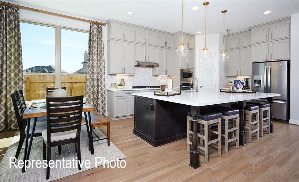 Expansive kitchen featuring a large central island with seating, light wood-finish flooring, light gray cabinetry, stainless steel appliances, and pendant lighting Expansive kitchen featuring a large central island with seating, light wood-finish flooring, light gray cabinetry, stainless steel appliances, and pendant lighting