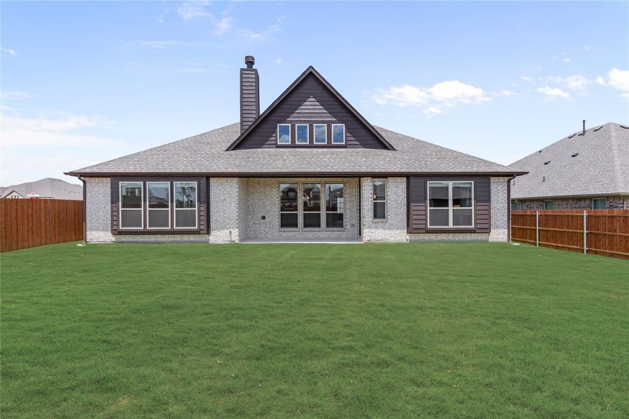 Rear exterior of brick home with chimney, large windows, covered patio, and fenced backyard with green lawn Rear exterior of brick home with chimney, large windows, covered patio, and fenced backyard with green lawn
