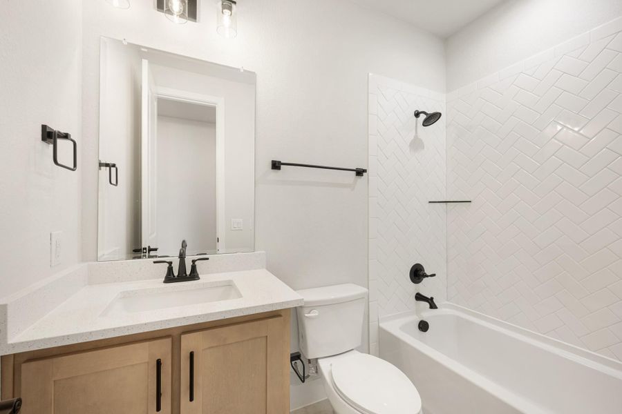 Bathroom with wood vanity, white quartz countertop, and tub-shower combo with herringbone tile and black fixtures Bathroom with wood vanity, white quartz countertop, and tub-shower combo with herringbone tile and black fixtures