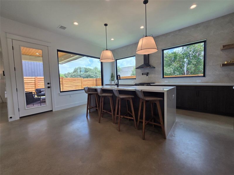 Full wall of backsplash tile surrounding the huge windows, range hood, pot filler, reclaimed wood accent shelving, waterfall island countertop.