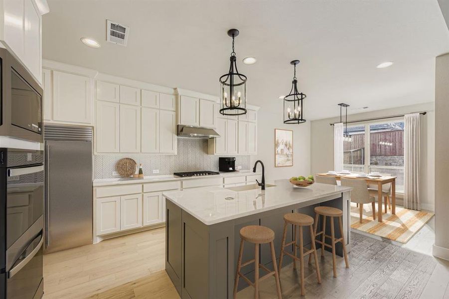Virtually staged photo - Kitchen featuring light wood-style flooring, two tone cabinetry, a kitchen bar, a center island with sink, and built in appliances