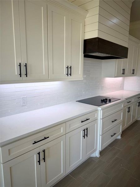 Kitchen featuring white cabinetry, decorative backsplash, light stone countertops, and black electric cooktop Kitchen featuring white cabinetry, decorative backsplash, light stone countertops, and black electric cooktop
