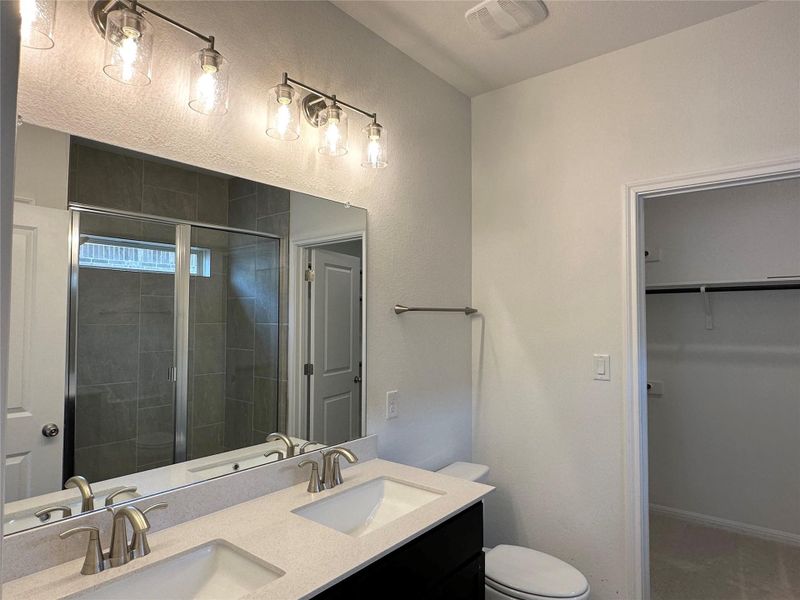 Full bathroom with a stall shower, double vanity, and a walk in closet