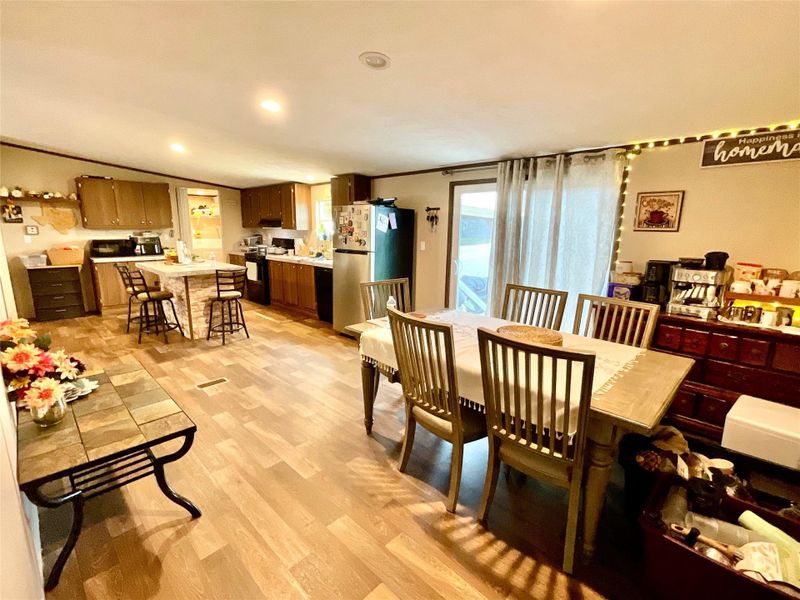 Open-concept interior featuring wood-finish flooring, recessed lighting, a kitchen island with seating, and a dining area with direct outdoor access via a sliding glass door