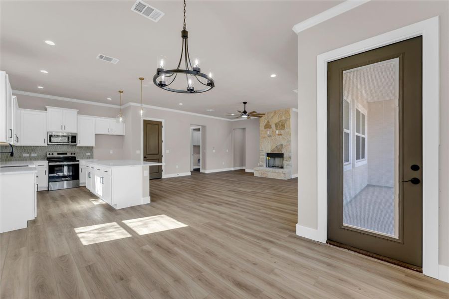 Kitchen featuring crown molding, suspended lighting, white cabinets, open floor plan, and stainless steel appliances
