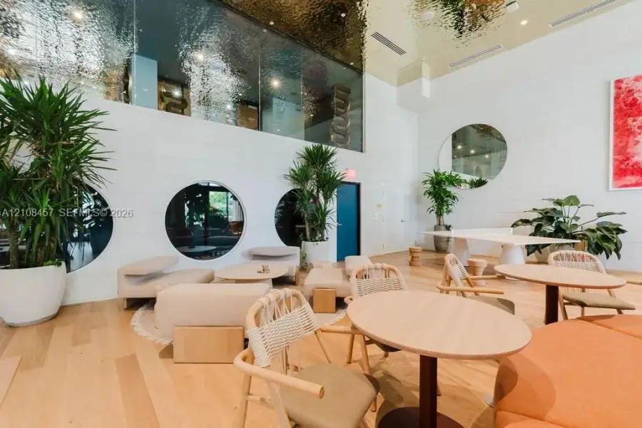 Expansive common area featuring high ceilings with a metallic finish, light wood-finish flooring, circular windows, and a large round wall mirror Expansive common area featuring high ceilings with a metallic finish, light wood-finish flooring, circular windows, and a large round wall mirror