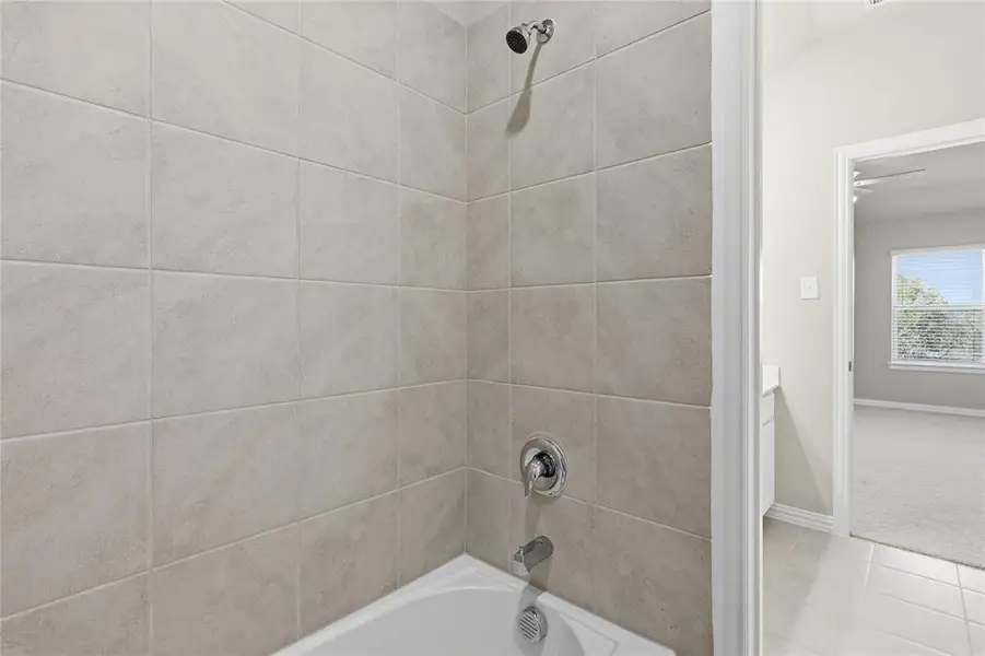 Tub-shower combination featuring light-toned rectangular tile surround and chrome fixtures