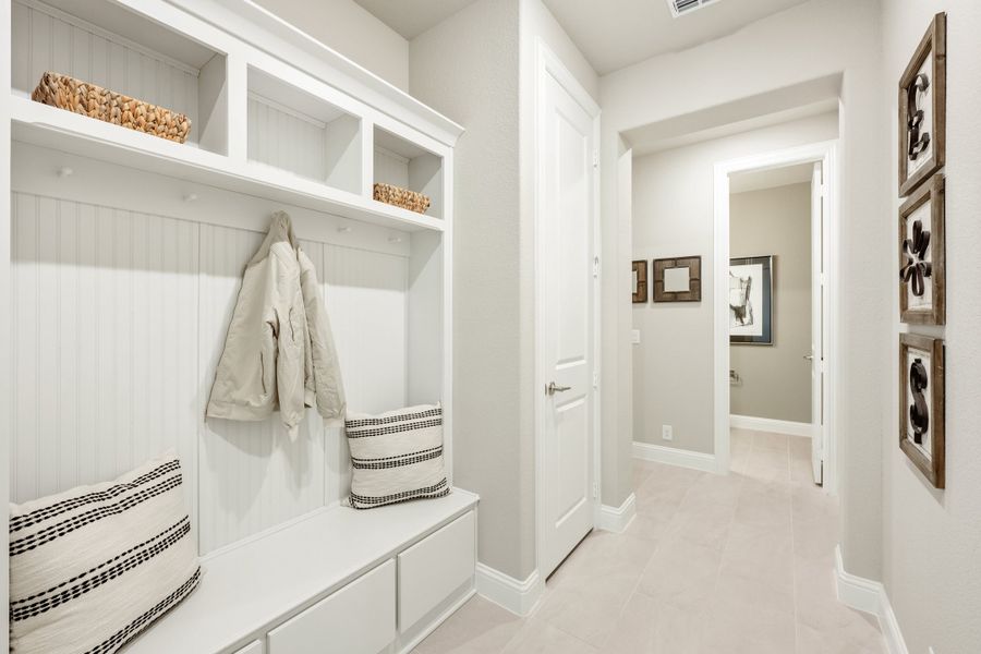 Mudroom with white built-in cubbies, coat hooks, bench seating, and open shelving with wicker baskets Mudroom with white built-in cubbies, coat hooks, bench seating, and open shelving with wicker baskets