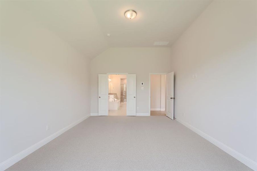 Unfurnished bedroom featuring carpet floors, ensuite bath, and vaulted ceiling