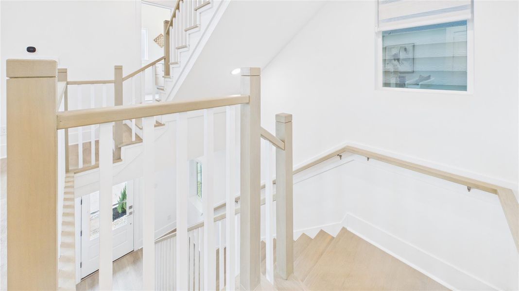 This photo showcases a bright, modern staircase with light wood railings and white accents. The space is well-lit with natural light from a window, creating an open and airy feel.