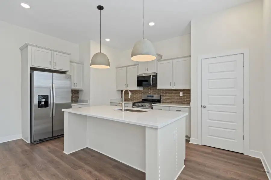 Kitchen with stainless steel appliances, white cabinetry, pendant lighting, a kitchen island with sink, and backsplash