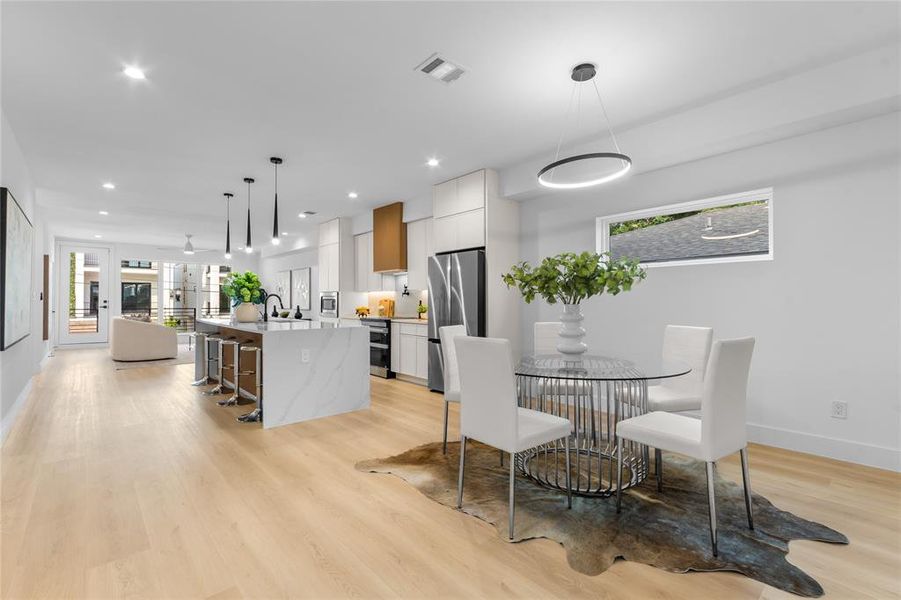 Open-concept living space featuring light wood-finish flooring, recessed lighting, a kitchen island with seating, a range hood, and a dining area with a modern chandelier Open-concept living space featuring light wood-finish flooring, recessed lighting, a kitchen island with seating, a range hood, and a dining area with a modern chandelier