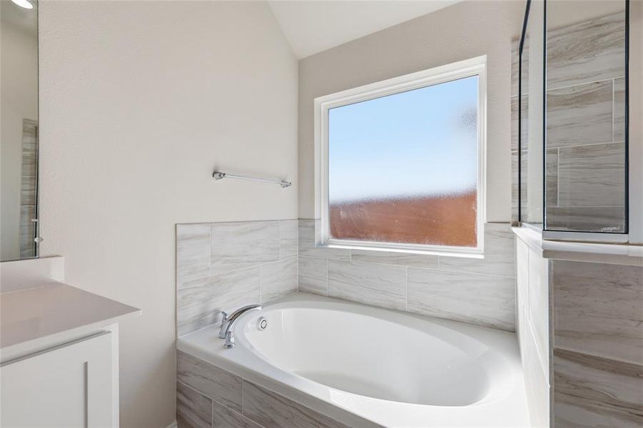 Soaking tub with chrome fixtures, surrounded by white and gray patterned wall tile