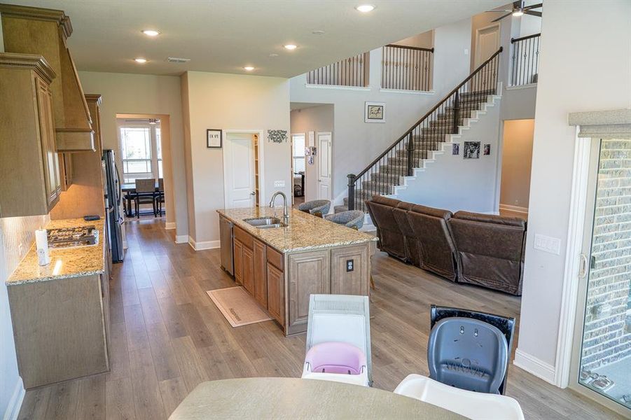 Kitchen featuring light stone counters, light wood-type flooring, a kitchen island with sink, brown cabinets, and a high ceiling