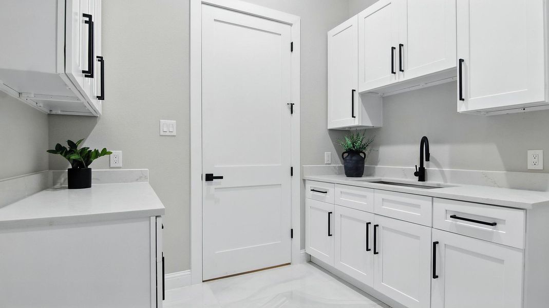 Enjoy a bright and beautifully finished laundry room designed for both convenience and style. This space features custom white cabinetry with bold matte black hardware, providing ample storage and a clean, contemporary aesthetic. The quartz countertops offer plenty of workspace for folding and organization, while the built-in sink adds functionality for easy cleanup. Elegant tile flooring and subtle décor touches give this room a polished, high-end feel—making everyday tasks effortless and stylish. Enjoy a bright and beautifully finished laundry room designed for both convenience and style. This space features custom white cabinetry with bold matte black hardware, providing ample storage and a clean, contemporary aesthetic. The quartz countertops offer plenty of workspace for folding and organization, while the built-in sink adds functionality for easy cleanup. Elegant tile flooring and subtle décor touches give this room a polished, high-end feel—making everyday tasks effortless and stylish.