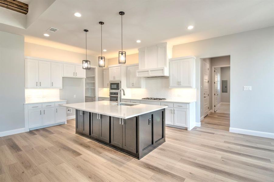 Kitchen with stainless steel microwave, a center island with sink, sink, gas stovetop, and white cabinetry