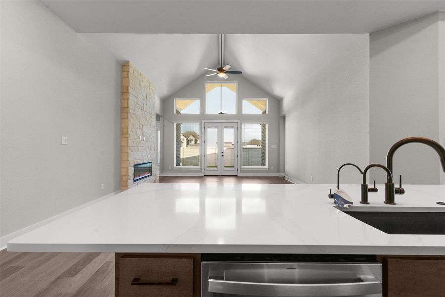 Kitchen featuring stainless steel dishwasher, open floor plan, a fireplace, light stone countertops, and light wood finished floors