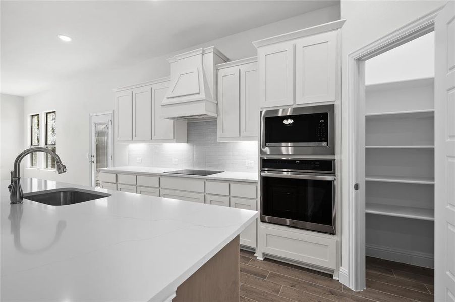 Kitchen with wood finish floors, stainless steel appliances, white cabinets, tasteful backsplash, and recessed lighting Kitchen with wood finish floors, stainless steel appliances, white cabinets, tasteful backsplash, and recessed lighting