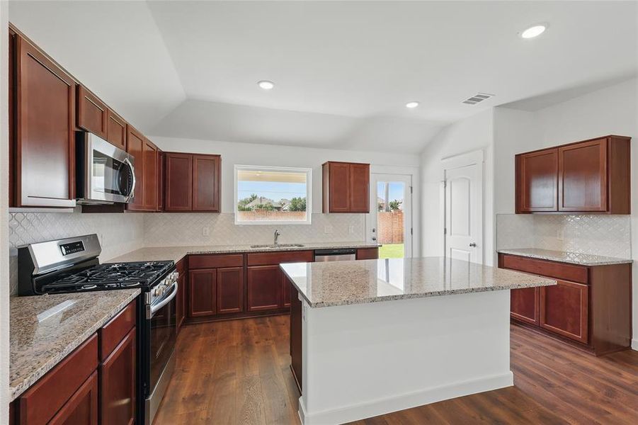 Kitchen featuring stainless steel appliances, lofted ceiling, light stone countertops, dark wood-type flooring, and decorative backsplash