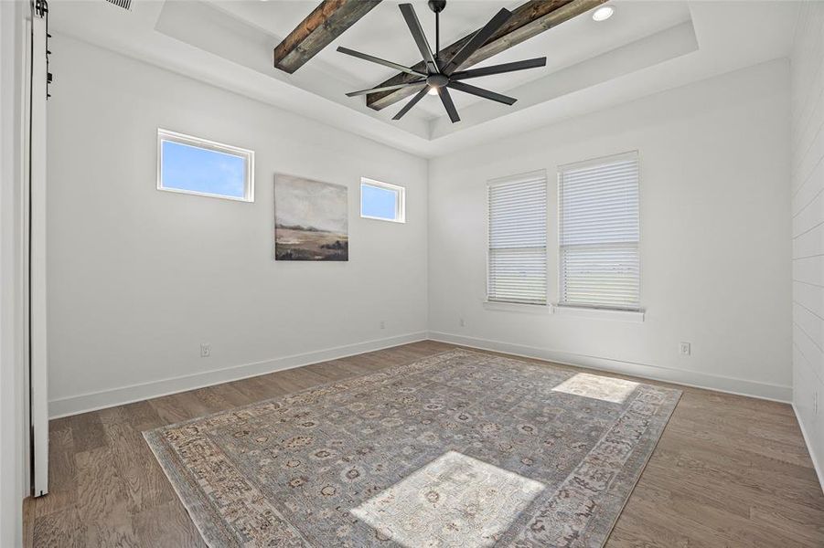 Unfurnished room with ceiling fan, beamed ceiling, dark hardwood / wood-style flooring, and a raised ceiling