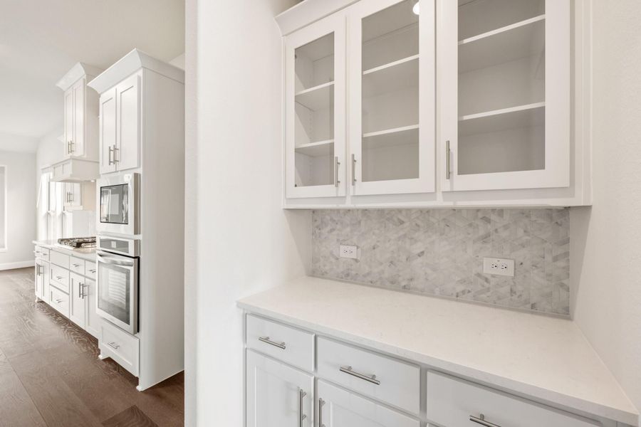 White kitchen with glass-front upper cabinets, marble tile backsplash, quartz countertops, and stainless steel double wall oven