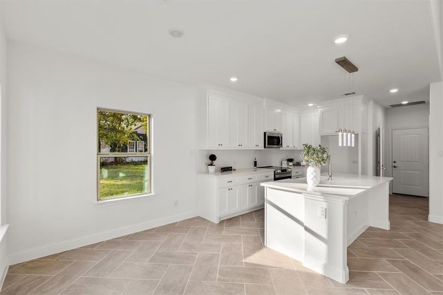 Kitchen featuring appliances with stainless steel finishes, white cabinets, decorative light fixtures, and an island with sink