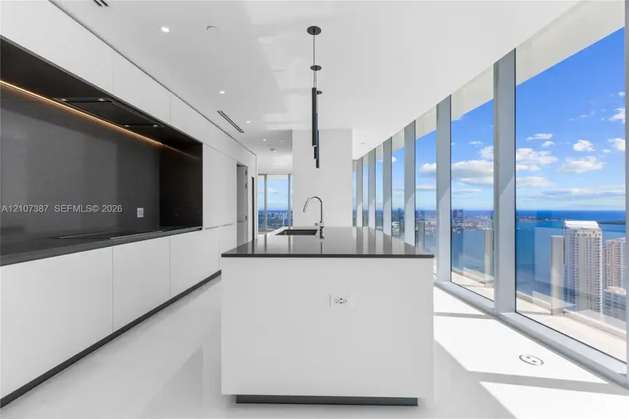 Contemporary kitchen featuring floor-to-ceiling windows, a center island with a dark stone countertop, minimalist flat-panel cabinetry, integrated recessed lighting, and polished stone flooring