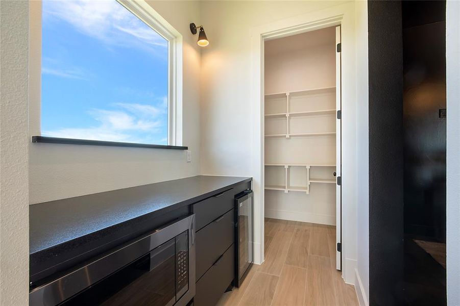 Bar area with stainless steel microwave, beverage cooler, dark countertops, and light wood-style floors Bar area with stainless steel microwave, beverage cooler, dark countertops, and light wood-style floors