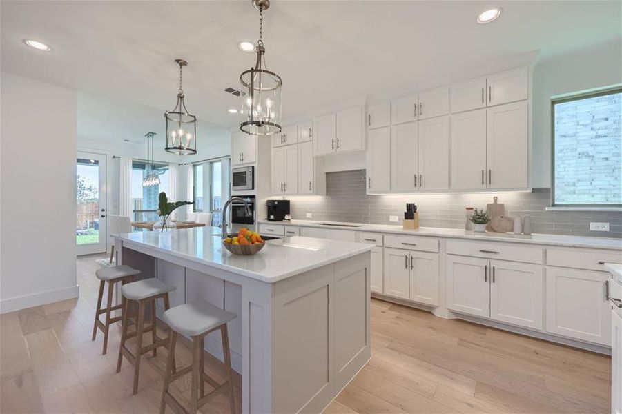 Virtually Staged Photo - Kitchen featuring light hardwood / wood-style flooring, a kitchen island with sink, stainless steel appliances, decorative backsplash, and decorative light fixtures