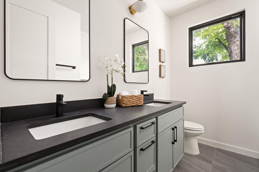 A well-appointed primary bathroom features dual vanities, modern fixtures, and a naturally illuminated window.