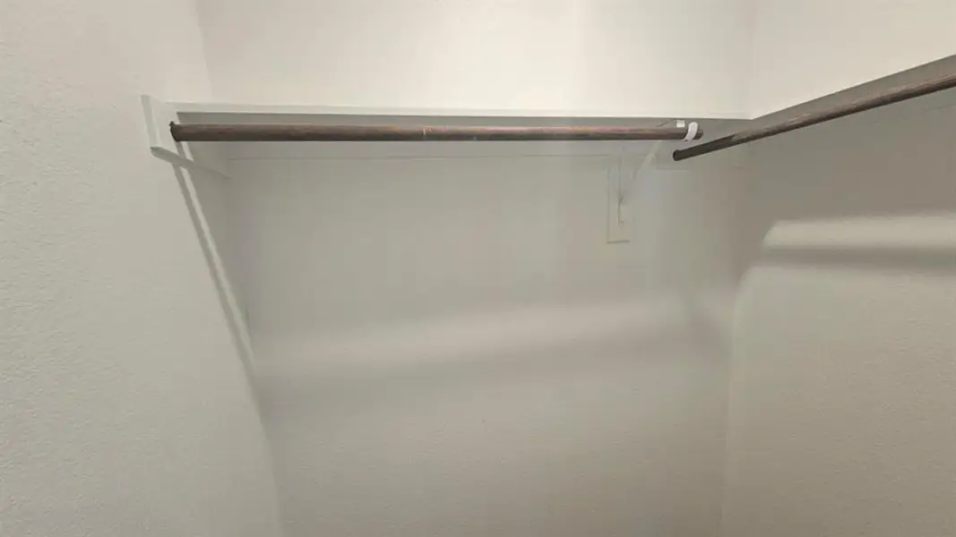 Walk-in closet featuring white painted walls, a built-in white shelf, and a dark-toned hanging rod Walk-in closet featuring white painted walls, a built-in white shelf, and a dark-toned hanging rod