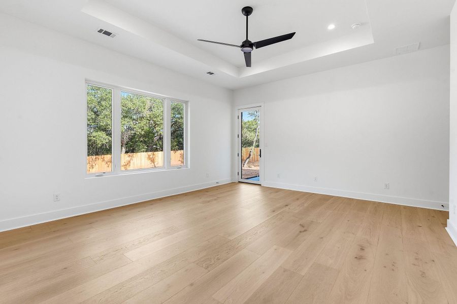 Rich hardwood flooring pairs with a recessed tray ceiling and glass doors in this airy space.