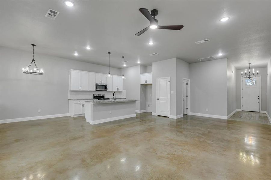 Unfurnished living room featuring a chandelier, concrete flooring, and a ceiling fan