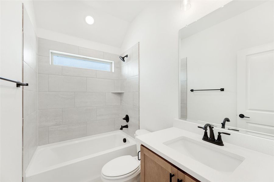 Bathroom with tiled tub-shower combo, white countertop vanity, and black fixtures Bathroom with tiled tub-shower combo, white countertop vanity, and black fixtures